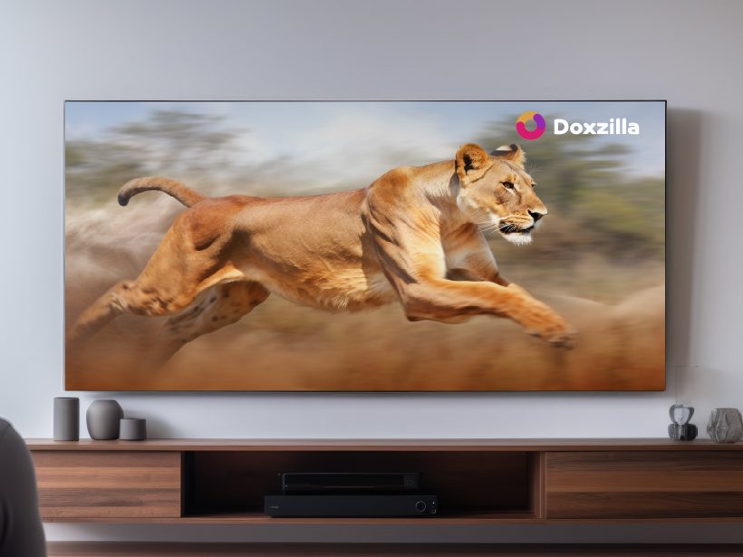 A large wall-mounted television in a living room showing a wildlife documentary of a running lion, with the Doxzilla logo in the corner of the screen