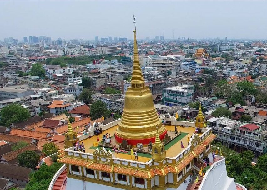 ภาพมุมสูงของเจดีย์สีทองและหลังคาวัดท่ามกลางย่านที่อยู่อาศัยของเมือง
